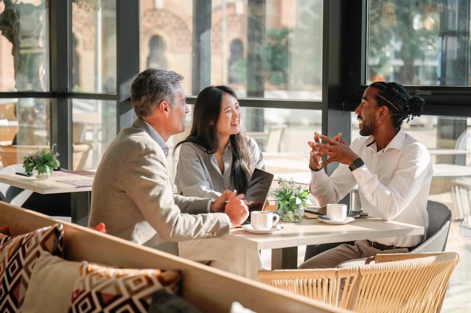 Drie collega's aan een tafel in gesprek, met koffie en een tablet erbij